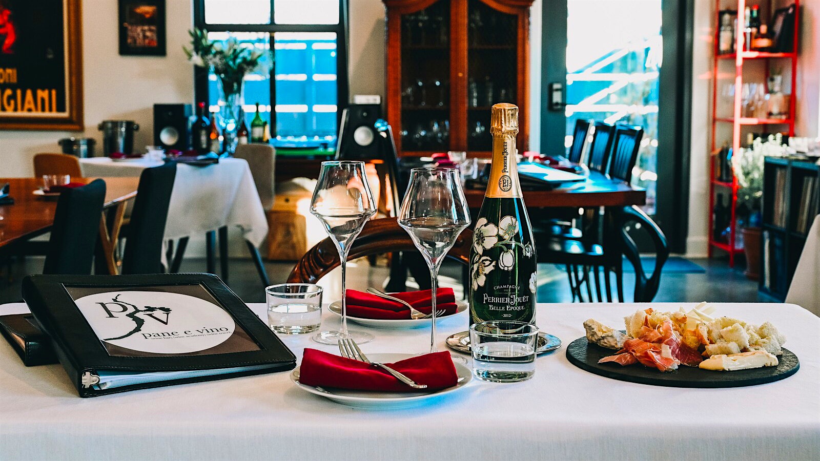 Glasses and dinnerplates on a table at Pane e Vino, with a bottle of Pierre Jouet and the wine list.